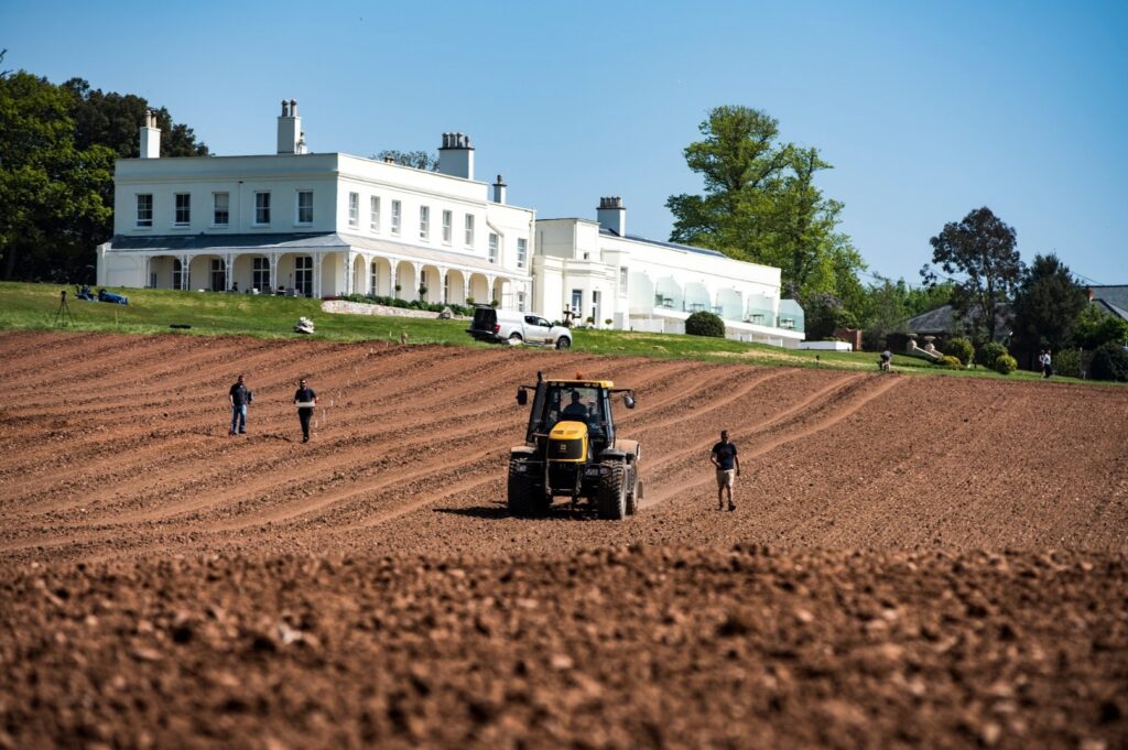 Lympstone Manor Hotel in the background with vineyard team and tractor in the foreground planting the vineyard.